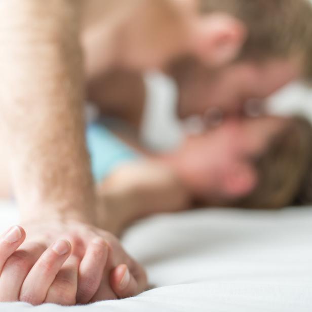 Ein Paar liegt im Bett und hält Händchen, während es sich küsst.