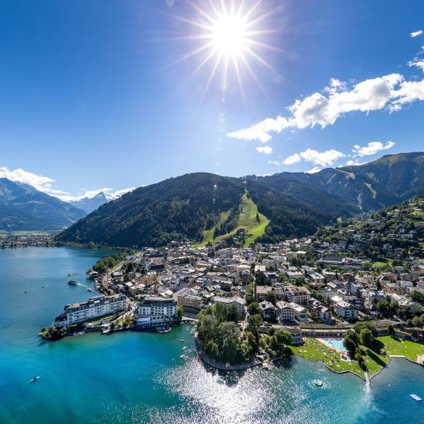 Luftaufnahme von Zell am See mit dem Zeller See und den umliegenden Bergen bei strahlendem Sonnenschein.
