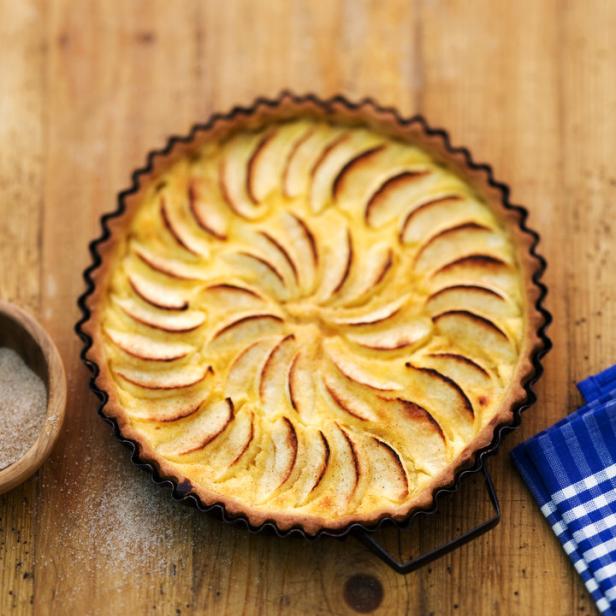 Frischer Apfelkuchen mit Schmand in der Backform auf einem Holztisch.