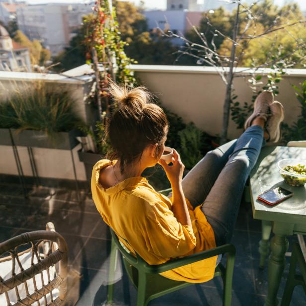 Eine Frau sitzt auf einem Balkon, trinkt Kaffee und genießt die Aussicht.
