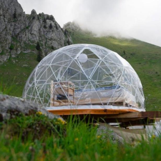 Eine transparente Kuppel dient als Hotelzimmer in einer Berglandschaft.