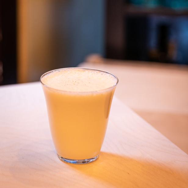 Ein Glas mit einem hellgelben Getränk steht auf einem Tisch.