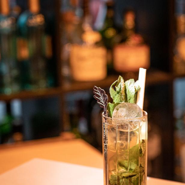 Ein Cocktail mit Eis und Minze steht auf einer Bar.