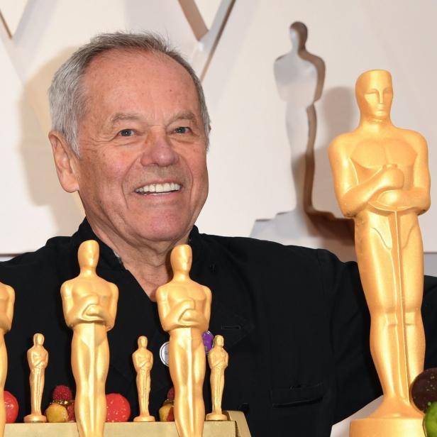 Wolfgang Puck posiert mit Oscar-Statuetten und Süßigkeiten bei einer Veranstaltung.