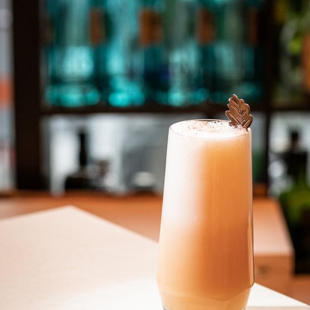 Ein cremiger Cocktail mit Blattdekoration steht auf einer Bar.