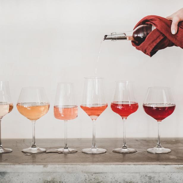 Eine Hand schenkt Wein in sechs Gläser mit unterschiedlichen Rosé- und Rottönen.