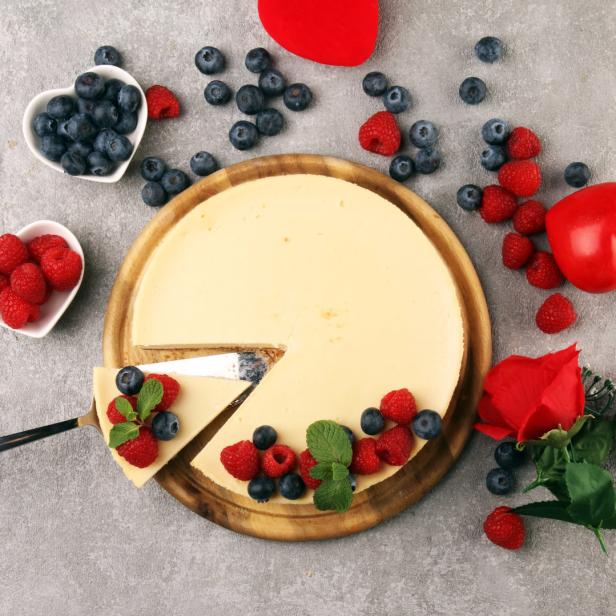 Ein Käsekuchen mit Beeren und einer Rose auf einem Holzteller.