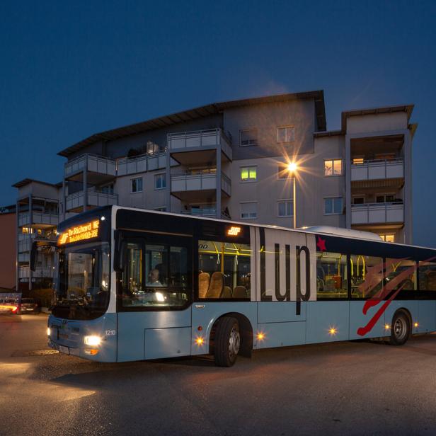 Ein Bus der Marke LUP steht nachts auf einer Straße vor Wohnhäusern.