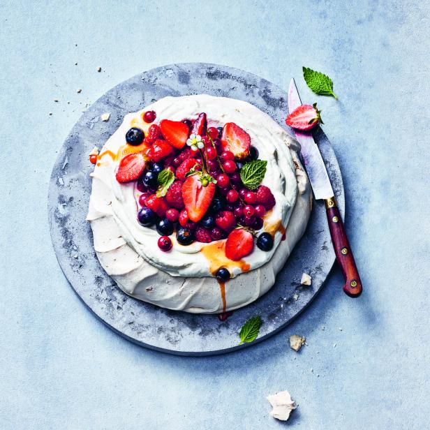 Eine Pavlova mit Schlagsahne und frischen Beeren auf einem grauen Teller.
