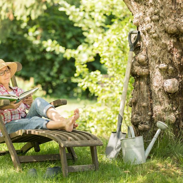 Eine Frau liest in einem Liegestuhl unter einem Baum im Garten.