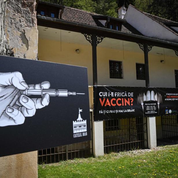 Eine Hand hält eine Spritze vor dem Schloss Bran, das für eine Impfkampagne wirbt.