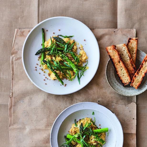 Zwei Teller mit Rührei, Spargel und Kräutern, dazu geröstetes Brot.