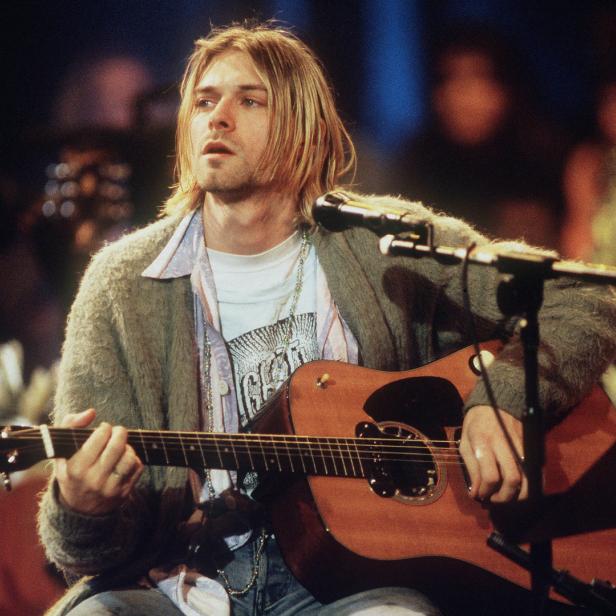 Kurt Cobain spielt auf der Bühne Akustikgitarre.