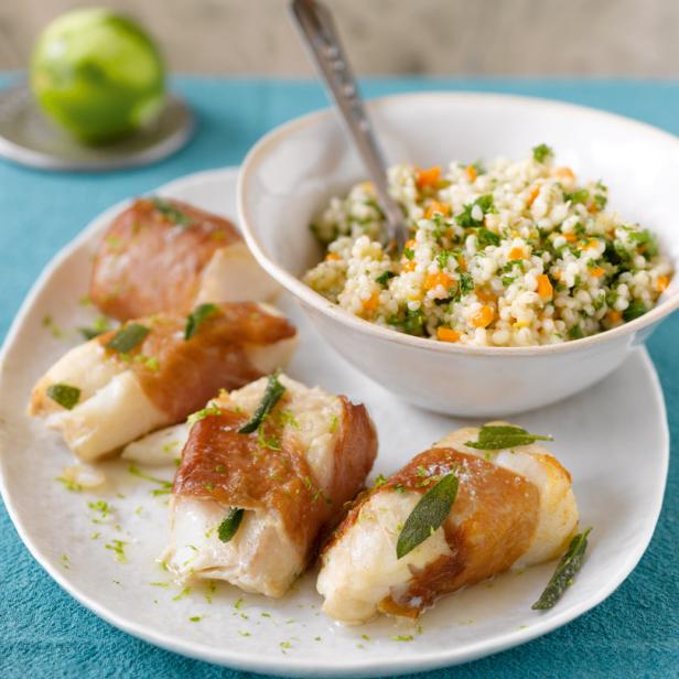 Auf einem Teller liegen mit Schinken umwickelte Fischstücke und ein Schälchen Couscous-Salat.