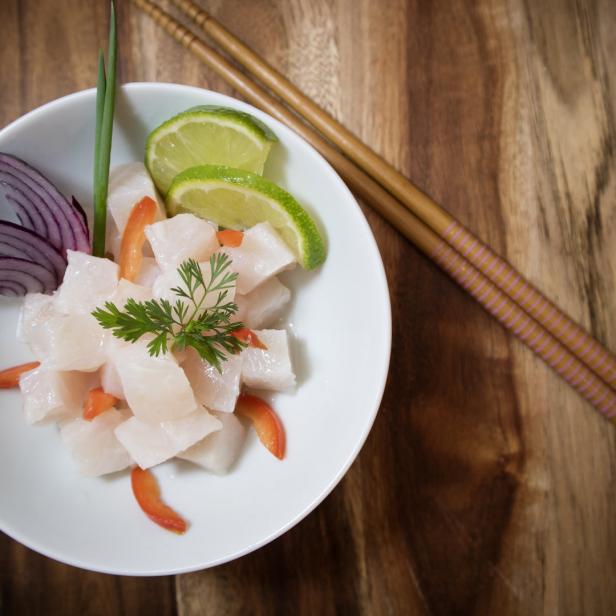 Ein Teller Ceviche mit Limetten, roter Zwiebel und Koriander auf einem Holztisch.