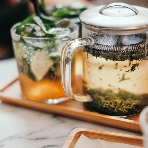 Ein Glas Mojito und eine Teekanne mit grünem Tee auf einem Holztablett.