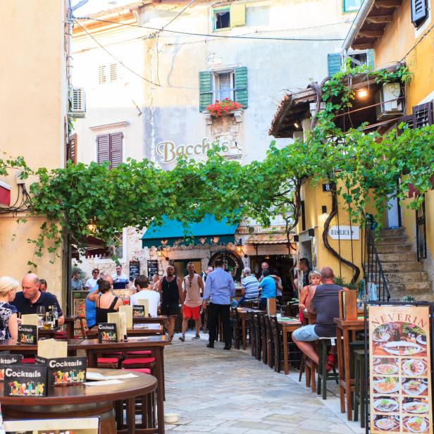 In einer Gasse sitzen Menschen in Restaurants unter Weinreben.