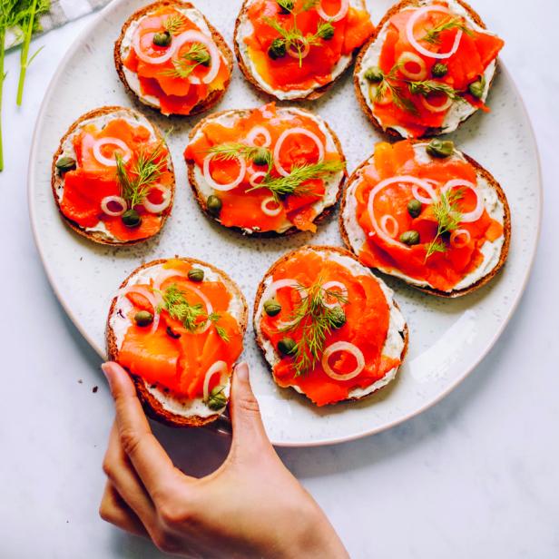Ein Teller mit Lachsschnittchen, belegt mit Frischkäse, Zwiebeln, Kapern und Dill.