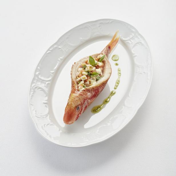 Ein gefüllter, roter Fisch liegt auf einem weißen Teller.