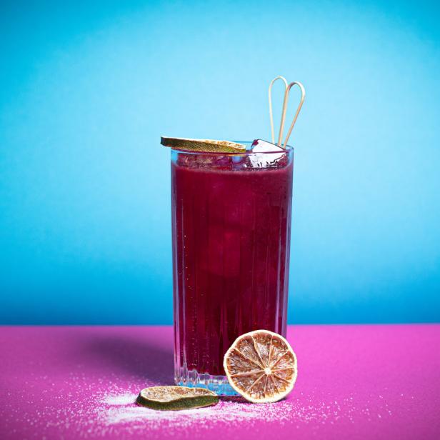 Ein Glas mit einem roten Getränk, Eis und einer Limettenscheibe vor blauem Hintergrund.