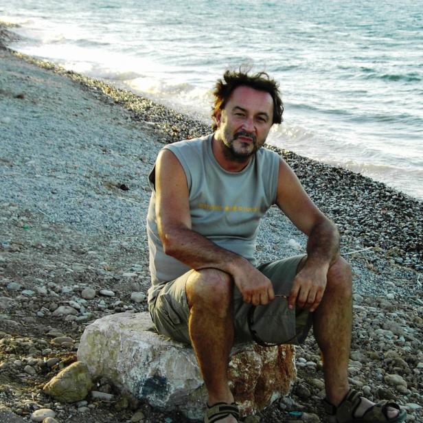 Rudi Treiber sitzt auf einem Stein am Strand.