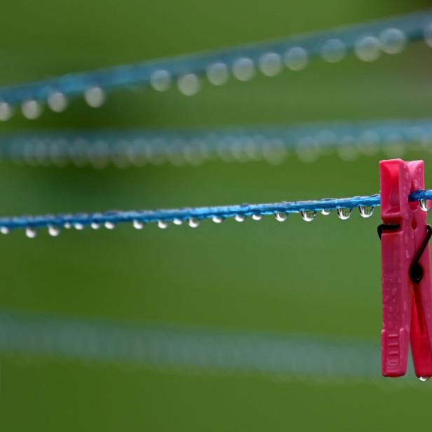 Zwei Wäscheklammern hängen an einer nassen Wäscheleine mit vielen Wassertropfen vor grünem Hintergrund.
