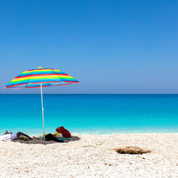 Blaues Meer, weißer Strand und ein bunter Sonnenschirm.