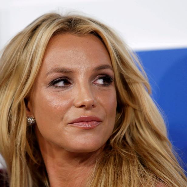 Britney Spears blickt mit blonden Haaren und Ohrringen zur Seite.