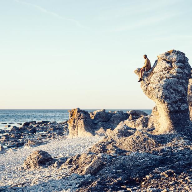 Ein Mann sitzt auf einem Felsen an der Küste und blickt aufs Meer.