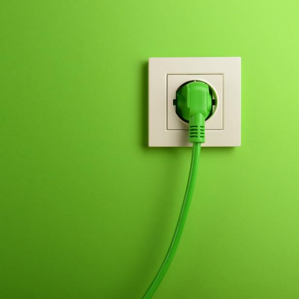Ein grüner Stecker steckt in einer Steckdose vor einer grünen Wand.