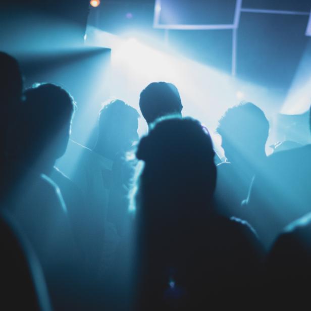 Silhouetten von Menschen stehen im blauen Licht einer Veranstaltung.