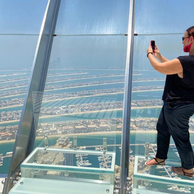 Eine Frau mit Maske fotografiert die Palmeninsel Jumeirah in Dubai von einer Aussichtsplattform aus.