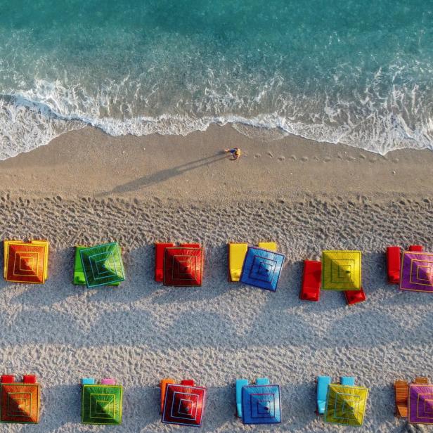 Luftaufnahme eines Strandes mit bunten Sonnenschirmen und einer Person im Wasser.
