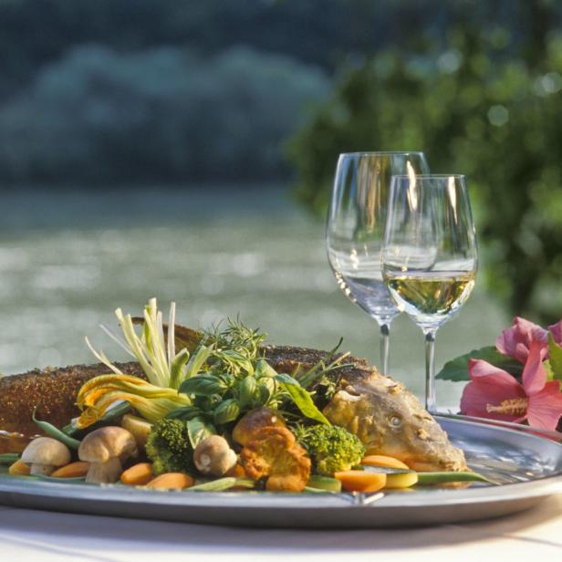 Ein zubereiteter Fisch mit Gemüse und zwei Gläsern Wein auf einem Tisch.
