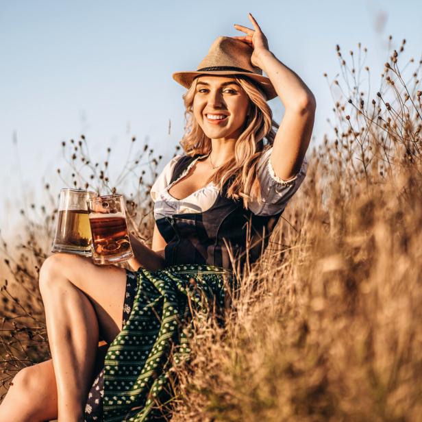 Eine Frau im Dirndl und mit Hut hält zwei Bierkrüge in der Hand.