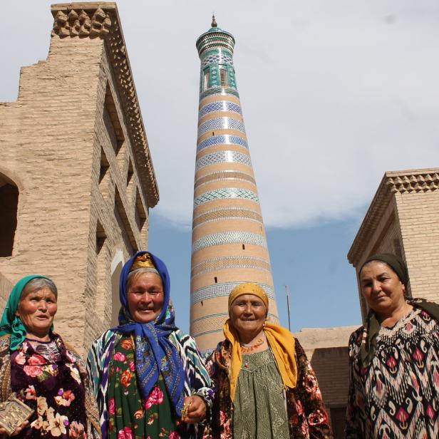 Vier Frauen in traditioneller Kleidung vor dem Islam-Hodscha-Minarett in Chiwa, Usbekistan.