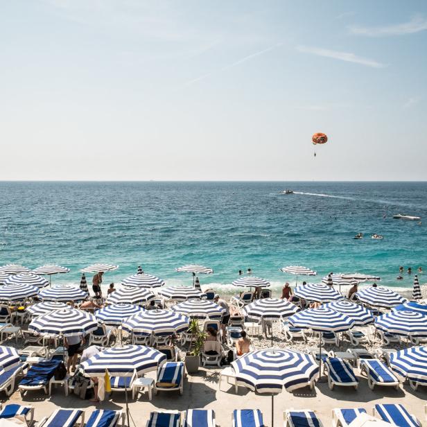 Ein Strand in Nizza mit blau-weiß gestreiften Sonnenschirmen und Badegästen.