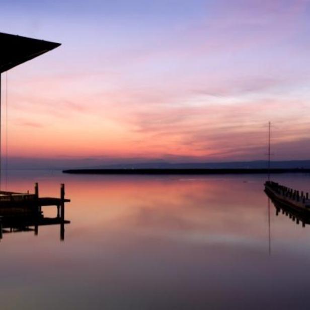 Ein Restaurant am Wasser mit Blick auf einen ruhigen See bei Sonnenuntergang.