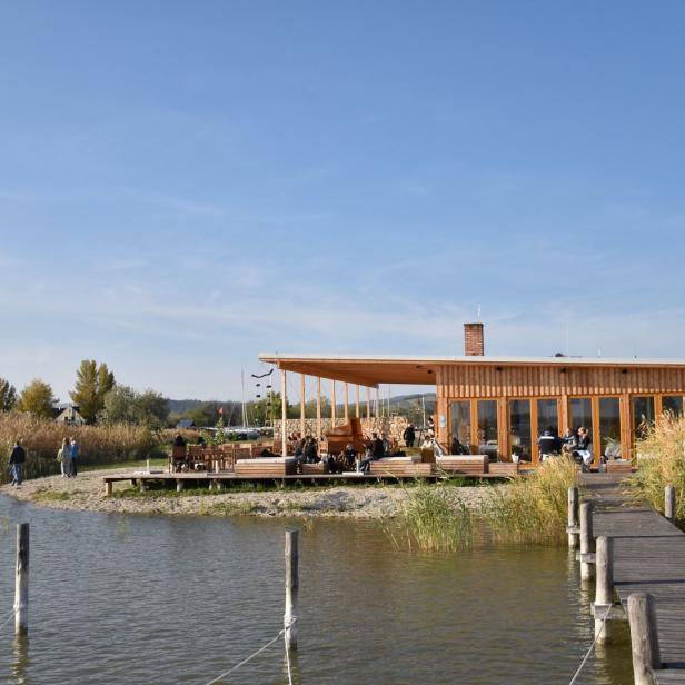 Ein Holzgebäude mit Terrasse steht am Ufer eines Sees, verbunden durch einen Steg.