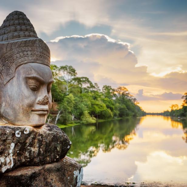 Ein steinerner Kopf bewacht einen Fluss in Angkor bei Sonnenuntergang.