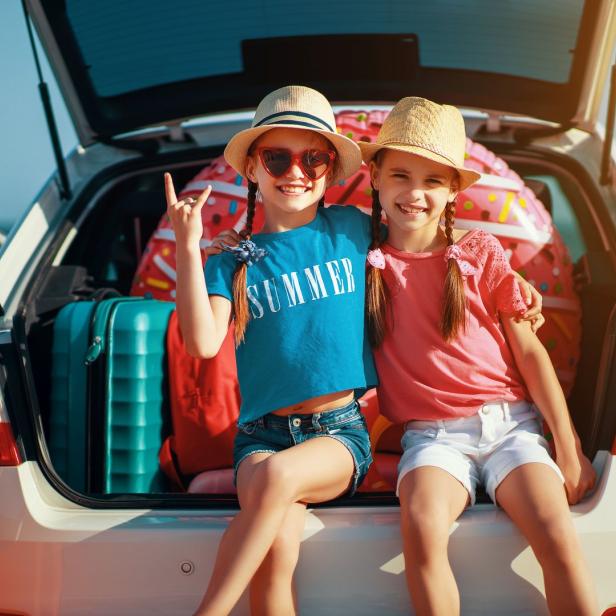 Zwei Mädchen sitzen auf dem Kofferraum eines Autos, bereit für den Sommerurlaub.