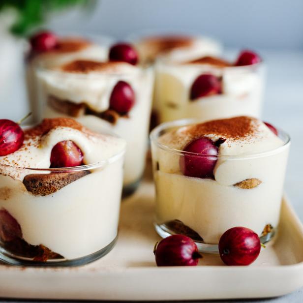 Mehrere Gläser Tiramisu mit Johannisbeeren und Kakaopulver stehen auf einem Tablett.