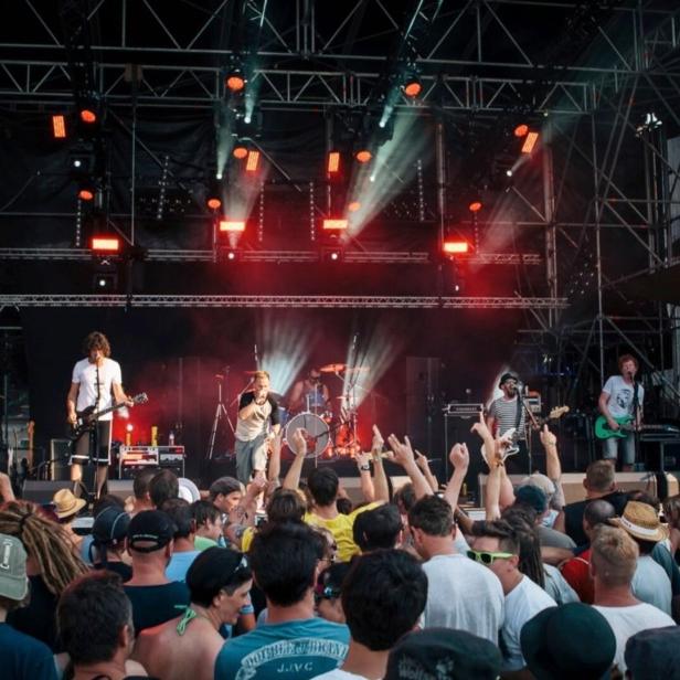 Rockband spielt vor großer jubelnder Menge auf einer Festivalbühne mit roten Lichtern.