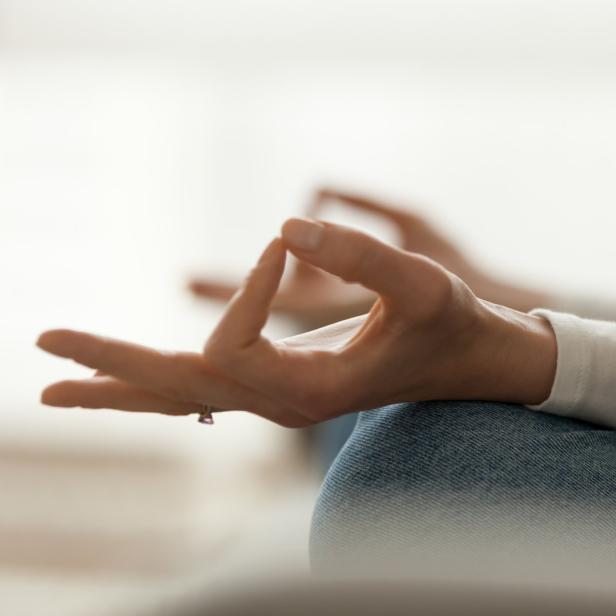 Eine Person meditiert mit gekreuzten Beinen und formt mit den Händen ein Mudra.