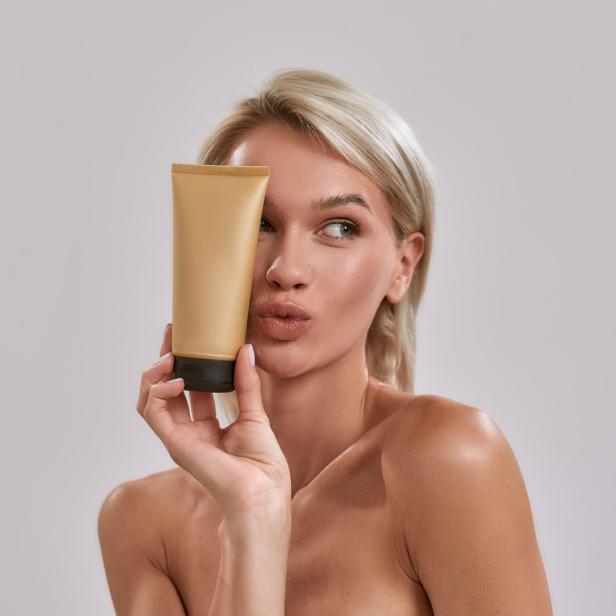 Eine Frau hält eine goldene Tube vor ihr Gesicht und schaut zur Seite.