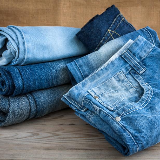 Ein Stapel gefalteter Jeanshosen in verschiedenen Blautönen liegt auf einem Holztisch.