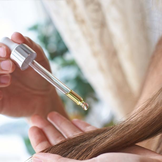 Eine Frau träufelt ein Öl mit einer Pipette auf ihr braunes Haar.