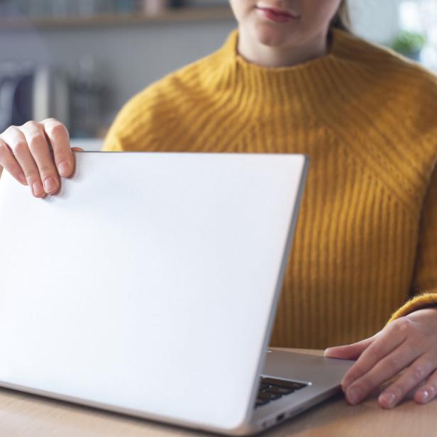 Eine Frau in einem gelben Pullover öffnet oder schließt einen Laptop.