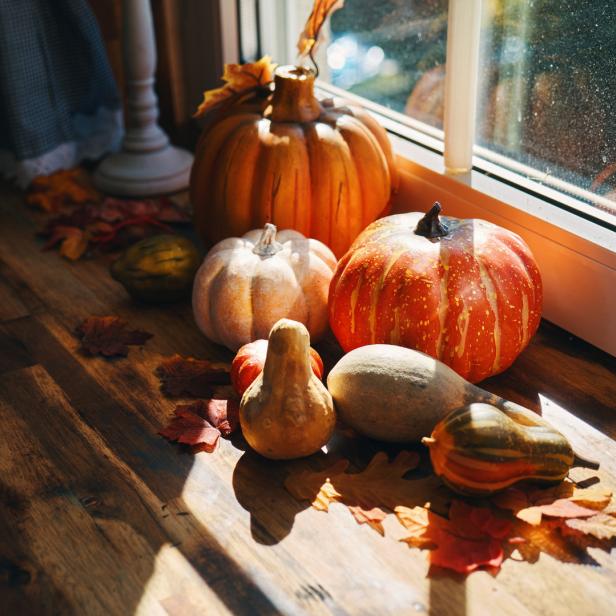 Verschiedene Kürbisse und Herbstblätter liegen auf einem Fensterbrett.