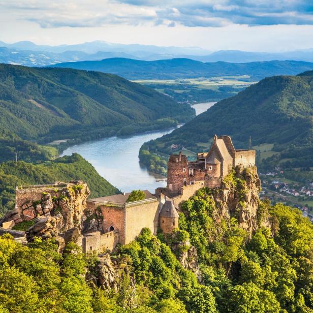 Die Burgruine Aggstein thront über der Donau, umgeben von bewaldeten Hügeln.
